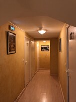 Un pasillo con piso de madera, paredes beige y puertas numeradas 20 y 21. Se observan cuadros enmarcados en las paredes y una lámpara en el techo.