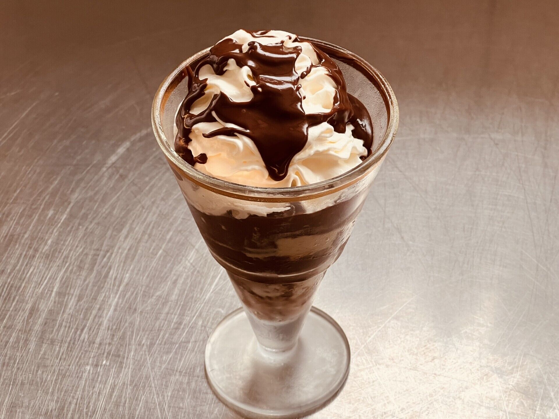 Postre en vaso transparente con crema batida y salsa de chocolate.