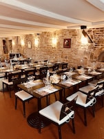 Um restaurante com várias mesas preparadas para refeições, paredes de pedra e uma lareira.