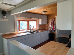 A compact kitchen with a window, wooden ceiling, and white cabinets.