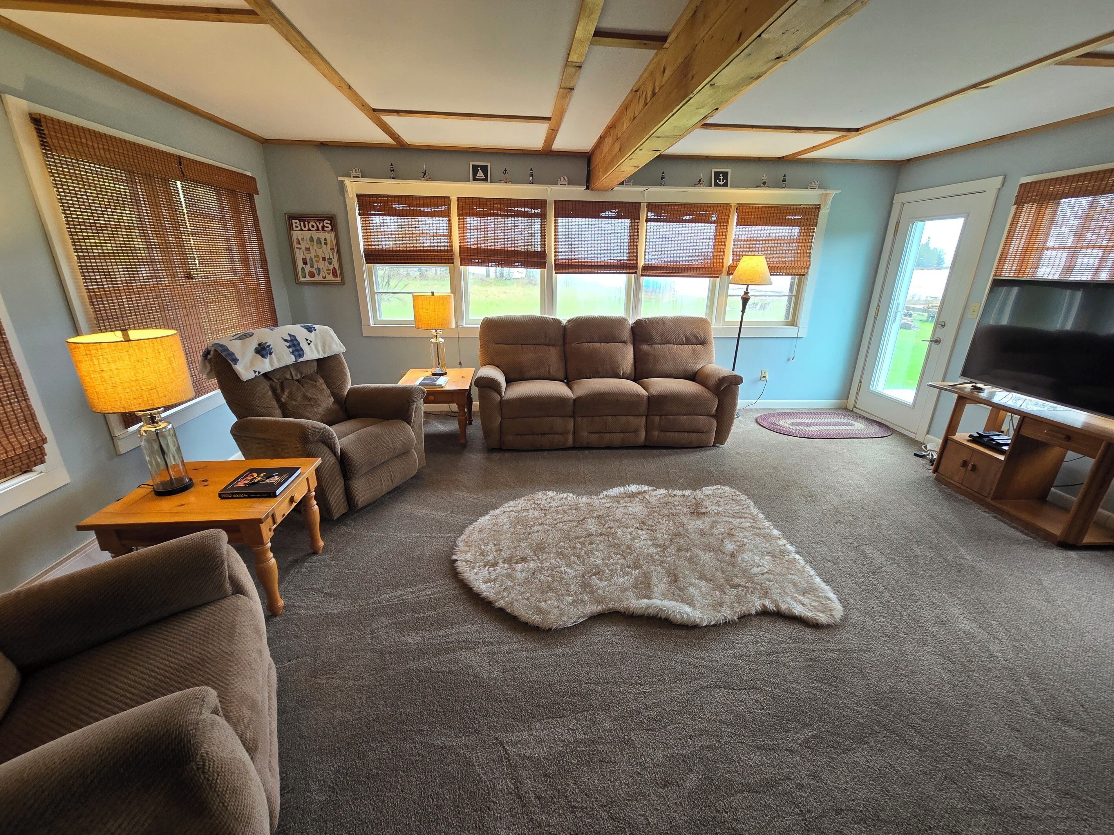 A living room with a sofa, two armchairs, a coffee table, a TV stand, and a large window with blinds.