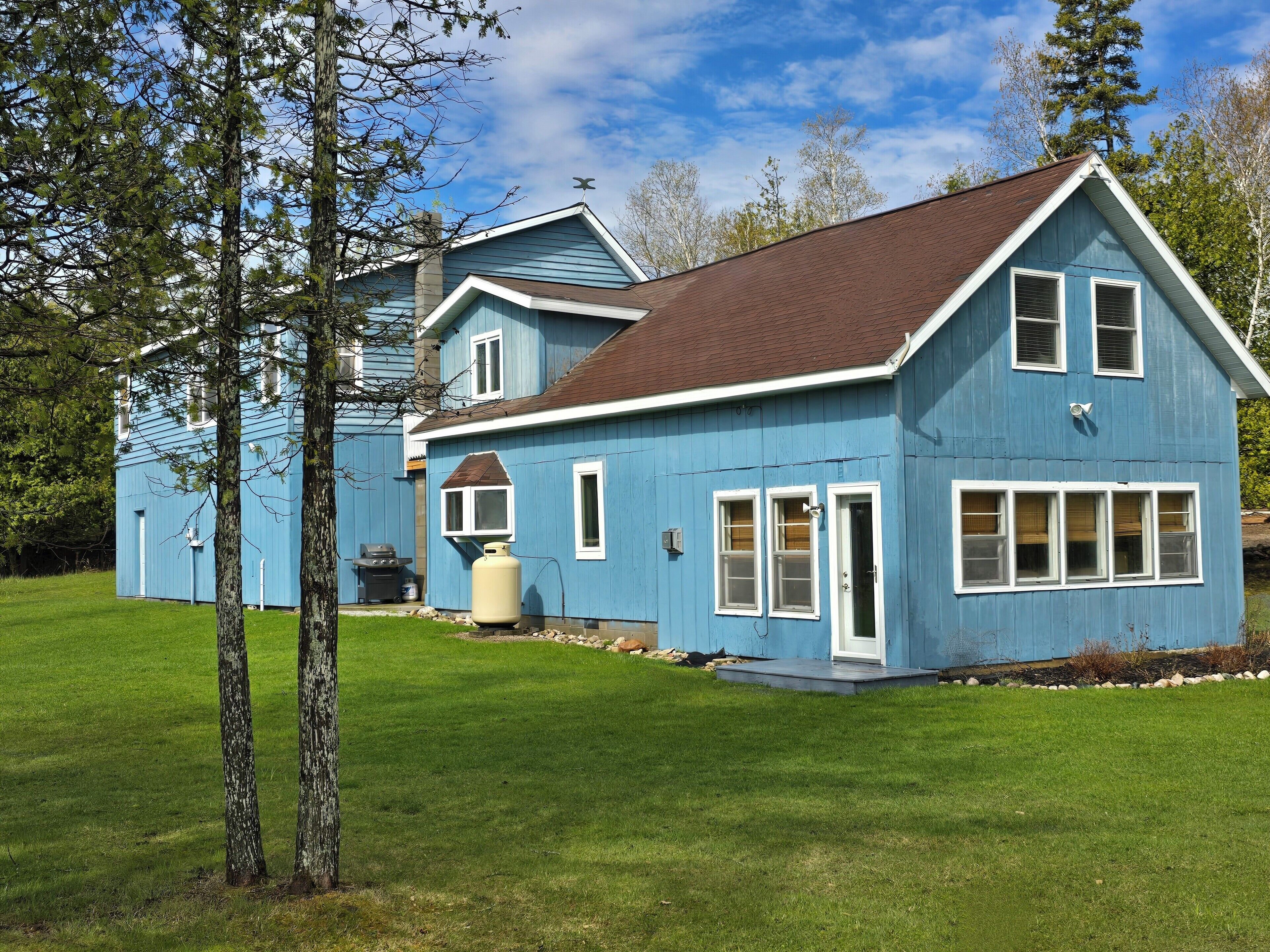 A large blue house with a brown roof, white trim, and a chimney.