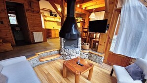 L’intérieur d’un chalet confortable, avec une cheminée en pierre, des meubles en bois et un téléviseur.