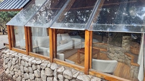 Une pièce moderne aux murs de pierre et aux poutres apparentes, entièrement vitrée, avec une cheminée en pierre et des sièges confortables.