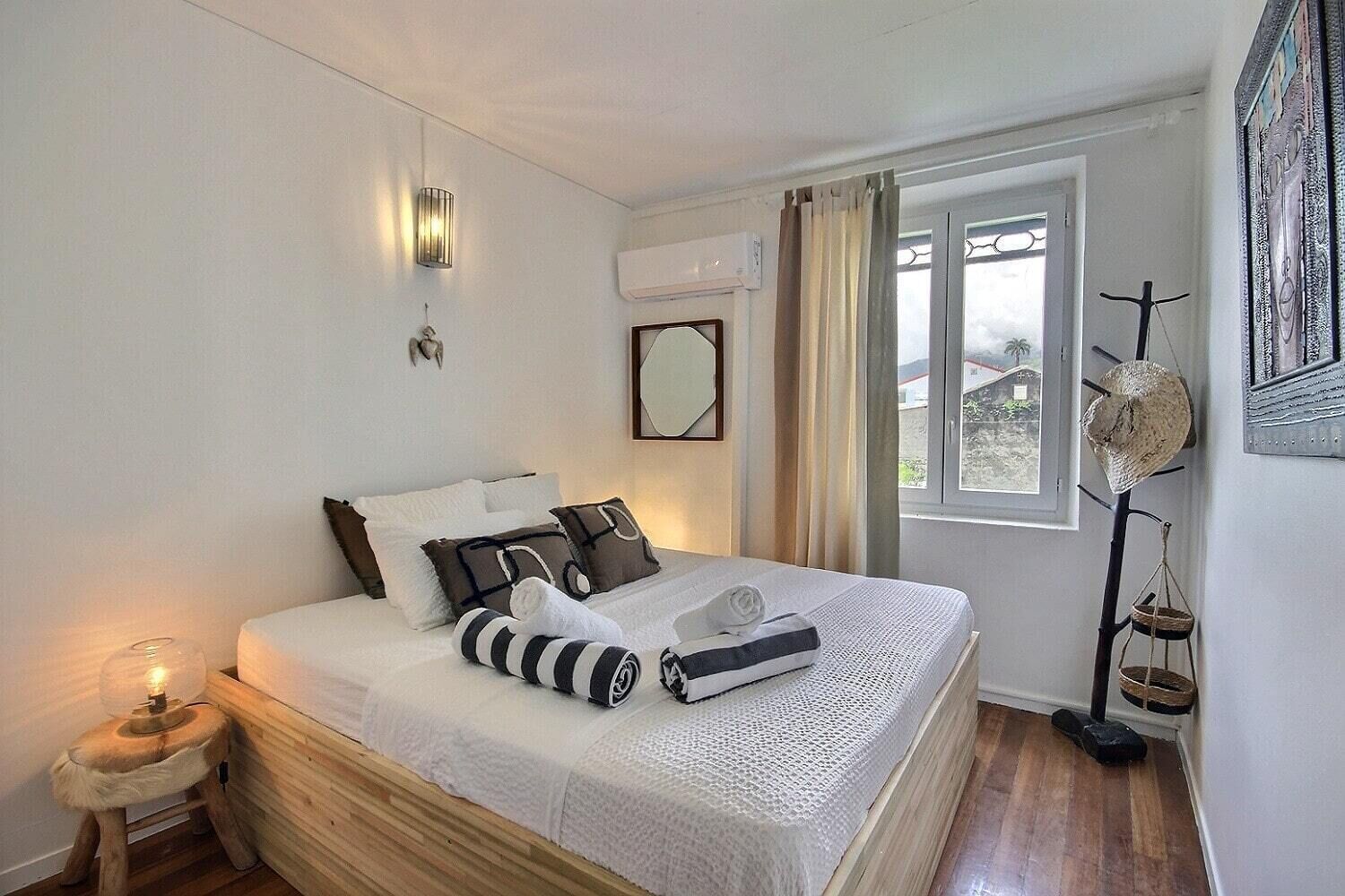 Een net opgemaakt bed met witte lakens en gestreepte kussens, een bedlamp en een houten nachtkastje.