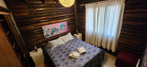 Una habitación acogedora con paredes de madera, una cama con colcha estampada, una mesita de noche, una lámpara y un cuadro en la pared.