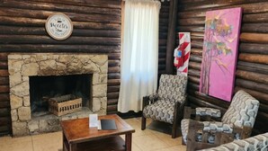 A rustic log cabin interior with a stone fireplace, patterned chairs, and a painting on the wall.