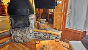 A stone fireplace with a TV mounted above it, a remote control, and a candle on a wooden table. - El Remanso - Arrayan Cabin, Bahía Manzano (Puerto Manzano)