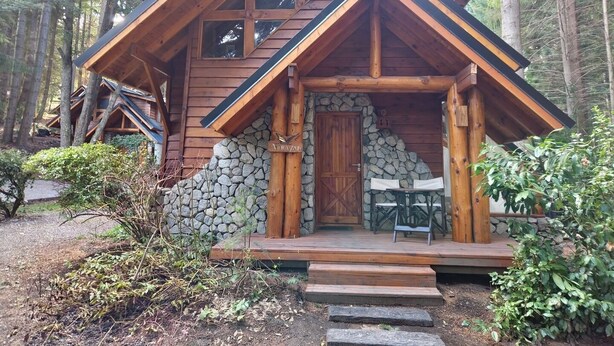 A cabin with a stone foundation, wooden exterior, and a porch with steps leading to a door. - El Remanso - Arrayan Cabin, Bahía Manzano (Puerto Manzano)