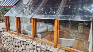 A modern glass-enclosed room with stone walls and wooden beams, featuring a stone fireplace and comfortable seating. - El Remanso - Arrayan Cabin, Bahía Manzano (Puerto Manzano)
