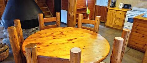 A wooden dining table with chairs, a kitchen area with wooden cabinets, a stove, and a chimney.