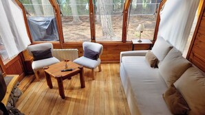 A cozy cabin interior with a wooden floor, a sofa, two chairs, a small table, and a lamp. - El Remanso - Arrayan Cabin, Bahía Manzano (Puerto Manzano)