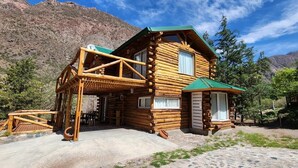 A log cabin with a balcony, a covered patio, and a mountain backdrop.