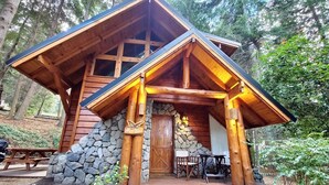 A rustic cabin with a stone foundation, wooden beams, and a porch with seating. - El Remanso - Radal Cabin, Manzano Bay (Puerto Manzano)