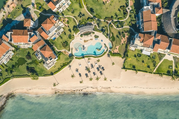 An aerial view of a resort with a central swimming pool, multiple buildings, and a beachfront.