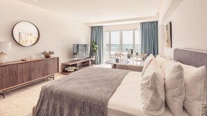 A modern hotel room with a large bed, a TV, a desk, and a balcony with a view of the sea. - Ocean View From Your Studio at Punta Palmera GC5 (Punta Cana)
