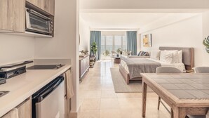 A modern kitchen with built-in appliances, a dining area with a wooden table, and a bedroom with a large bed and a view of the sea. - Ocean View From Your Studio at Punta Palmera GC5 (Punta Cana)