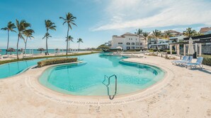 A resort pool with clear blue water, surrounded by palm trees and lounge chairs. - Ocean View From Your Studio at Punta Palmera GC5 (Punta Cana)