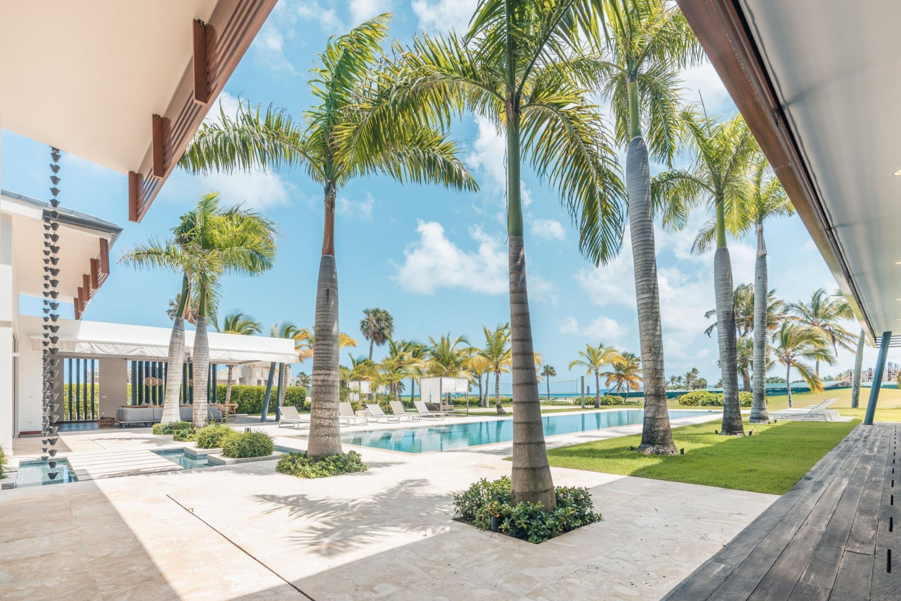 Un resort moderno con piscina, palmeras y una zona de patio cubierta.