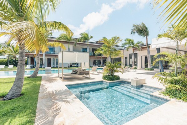 A modern resort with a swimming pool, lounge chairs, and palm trees.