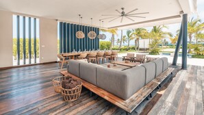 A spacious outdoor seating area with a long grey sofa, wooden tables, wicker chairs, and a ceiling fan.