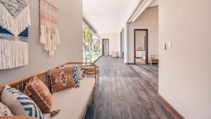 A hallway with a wooden floor, a sofa with cushions, and a wall with a macramé piece.