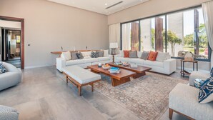 A spacious living room with a large sofa set, a coffee table, and a view of the outdoors through large windows.