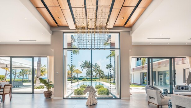 A spacious room with a large glass door leading to a pool area, wooden ceiling beams, and a modern chandelier.