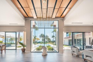 A spacious room with a large glass door leading to a pool area, wooden ceiling beams, and a modern chandelier. - Villa With Ocean View Maid Jacuzzi Cap Cana (Punta Cana)