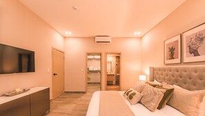 Quarto de hotel com cama, televisão, guarda-roupa e casa de banho visível através de uma porta aberta.
