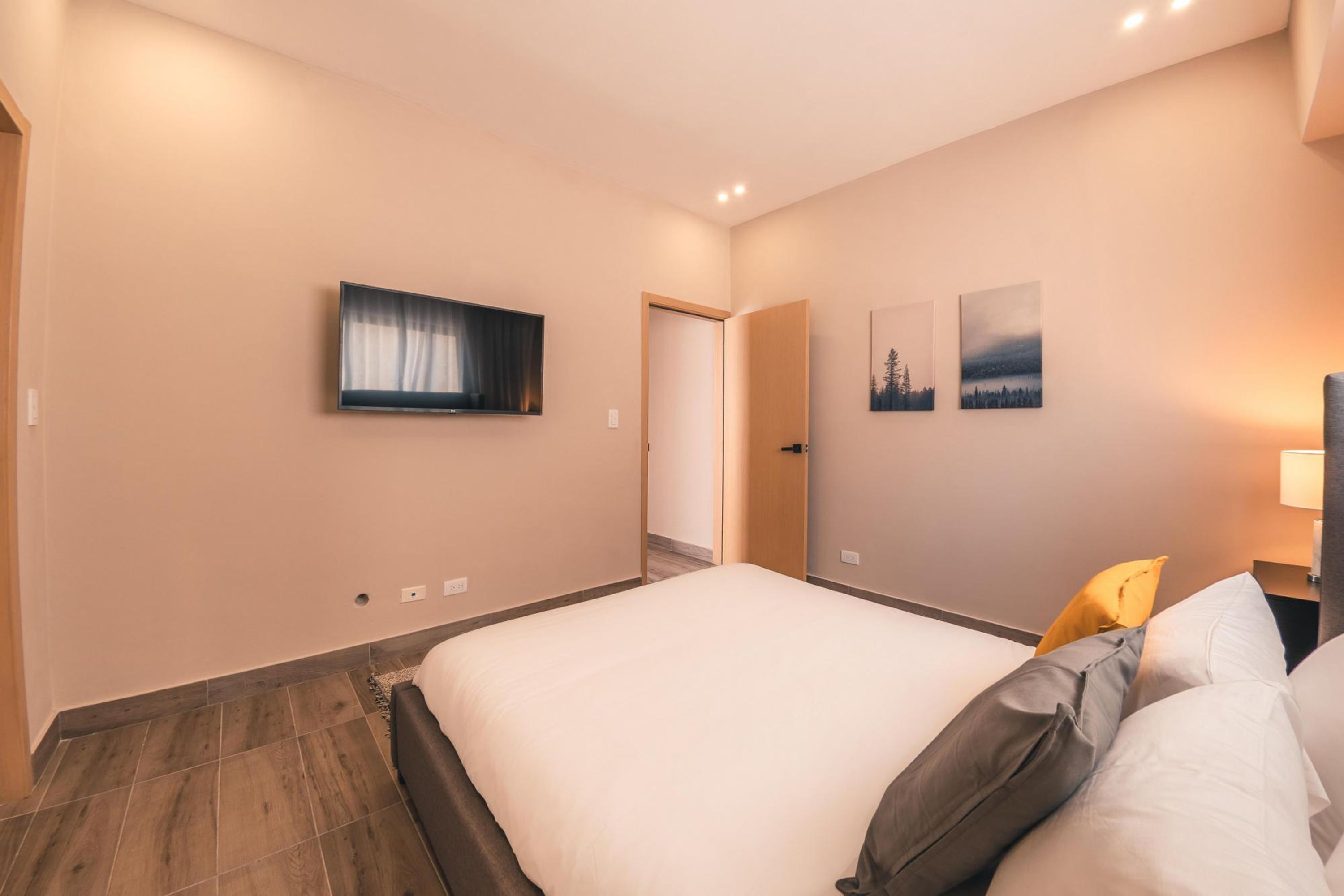 Ein Hotelzimmer mit einem großen Bett, einem flachbildfernseher an der Wand und zwei gerahmten Bildern an der Wand.