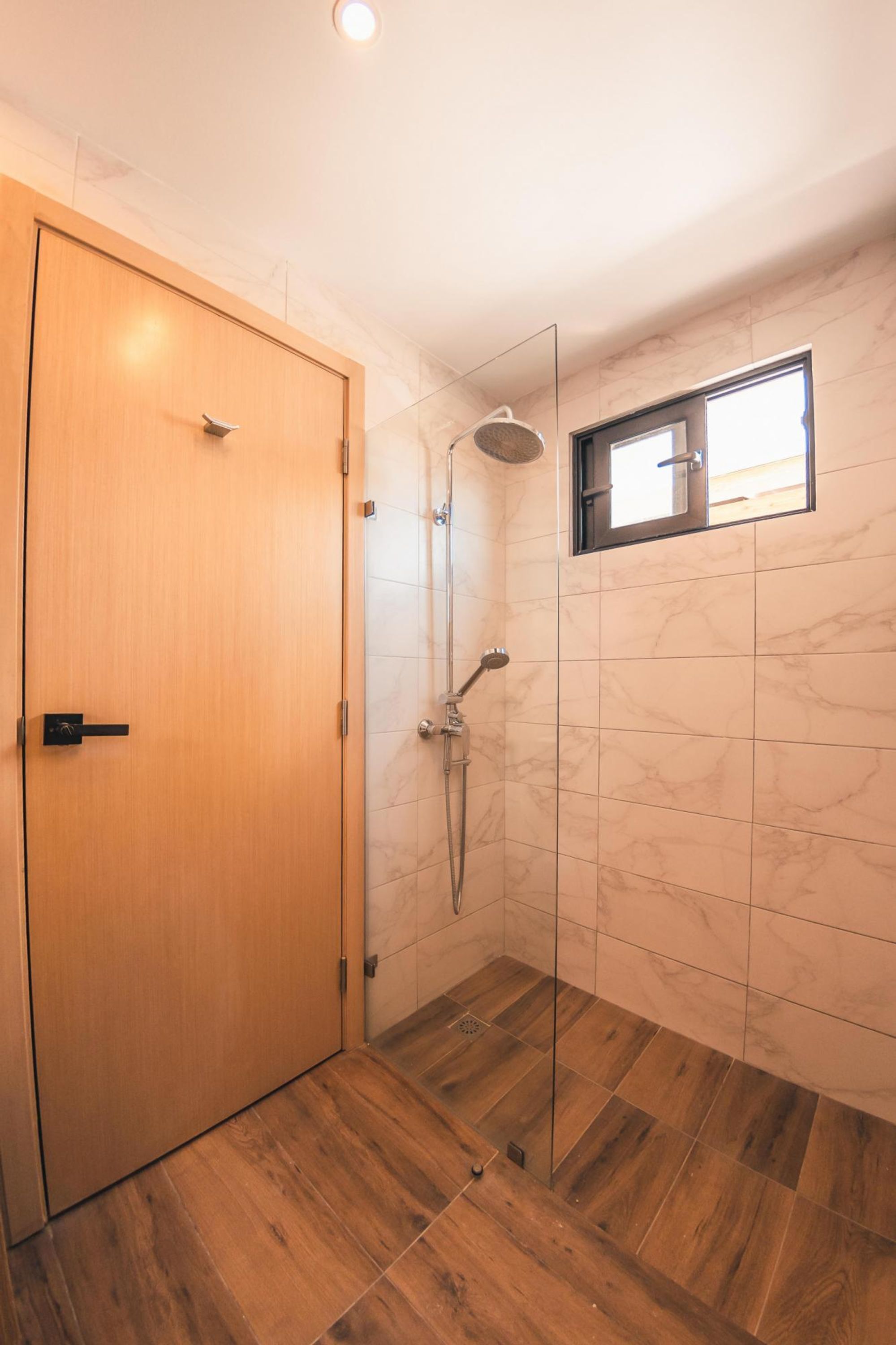 A bathroom with a wooden door, a shower with a glass enclosure, and a small window.