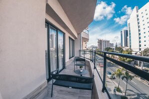 Un balcón con vistas a la ciudad, que incluye una mesa, sillas y una planta en maceta.