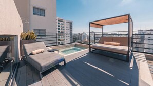 A rooftop terrace with a hot tub, lounge chairs, and a canopy seating area.