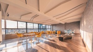 A spacious, modern lounge with large windows, wooden flooring, and yellow chairs.