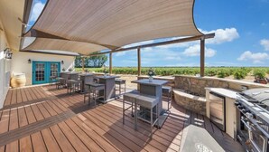 Una terraza de madera con mobiliario exterior, una parrilla y vistas a viñedos.