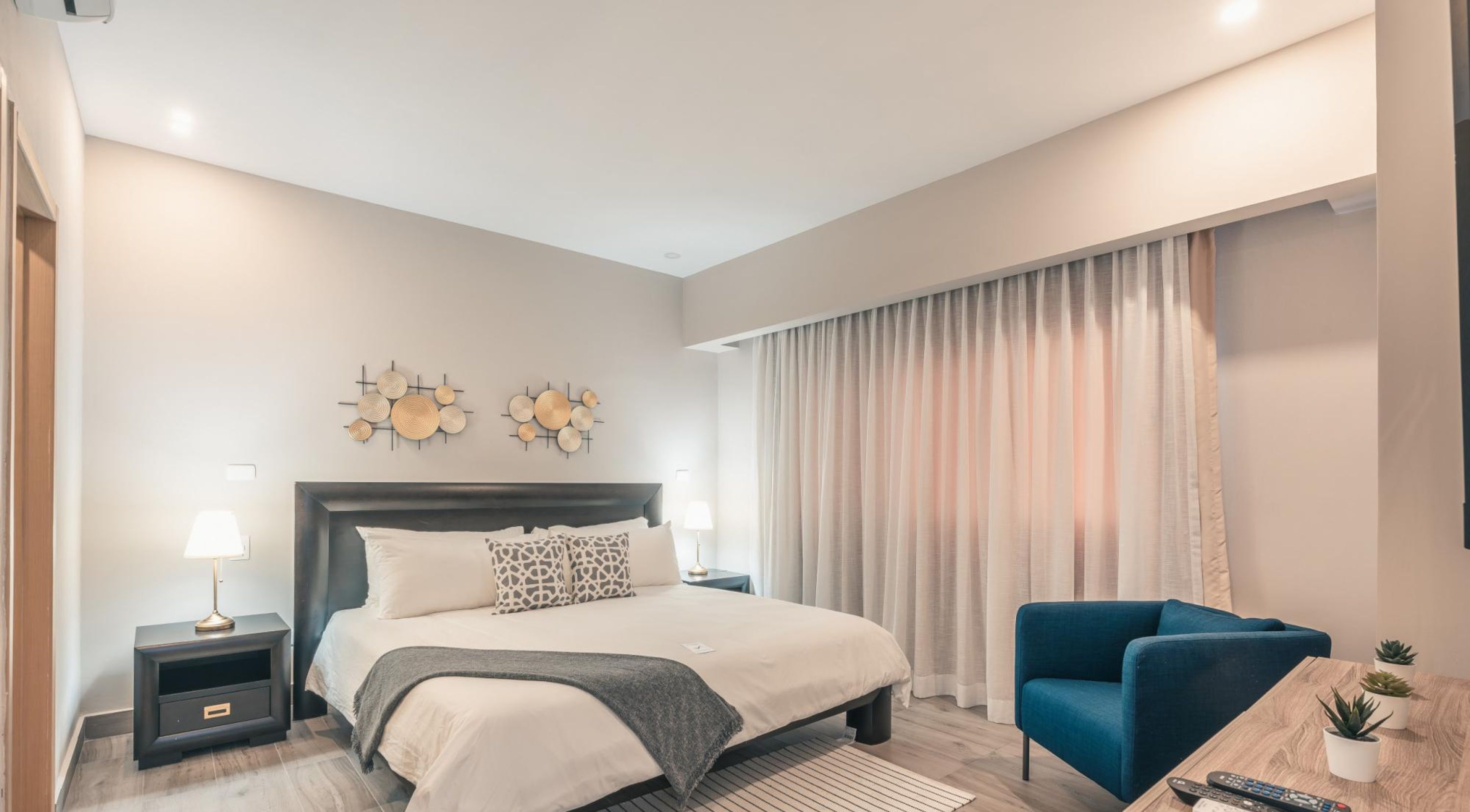 Un dormitorio moderno con cama, mesitas de noche, un sillón azul y una pequeña mesa con plantas.