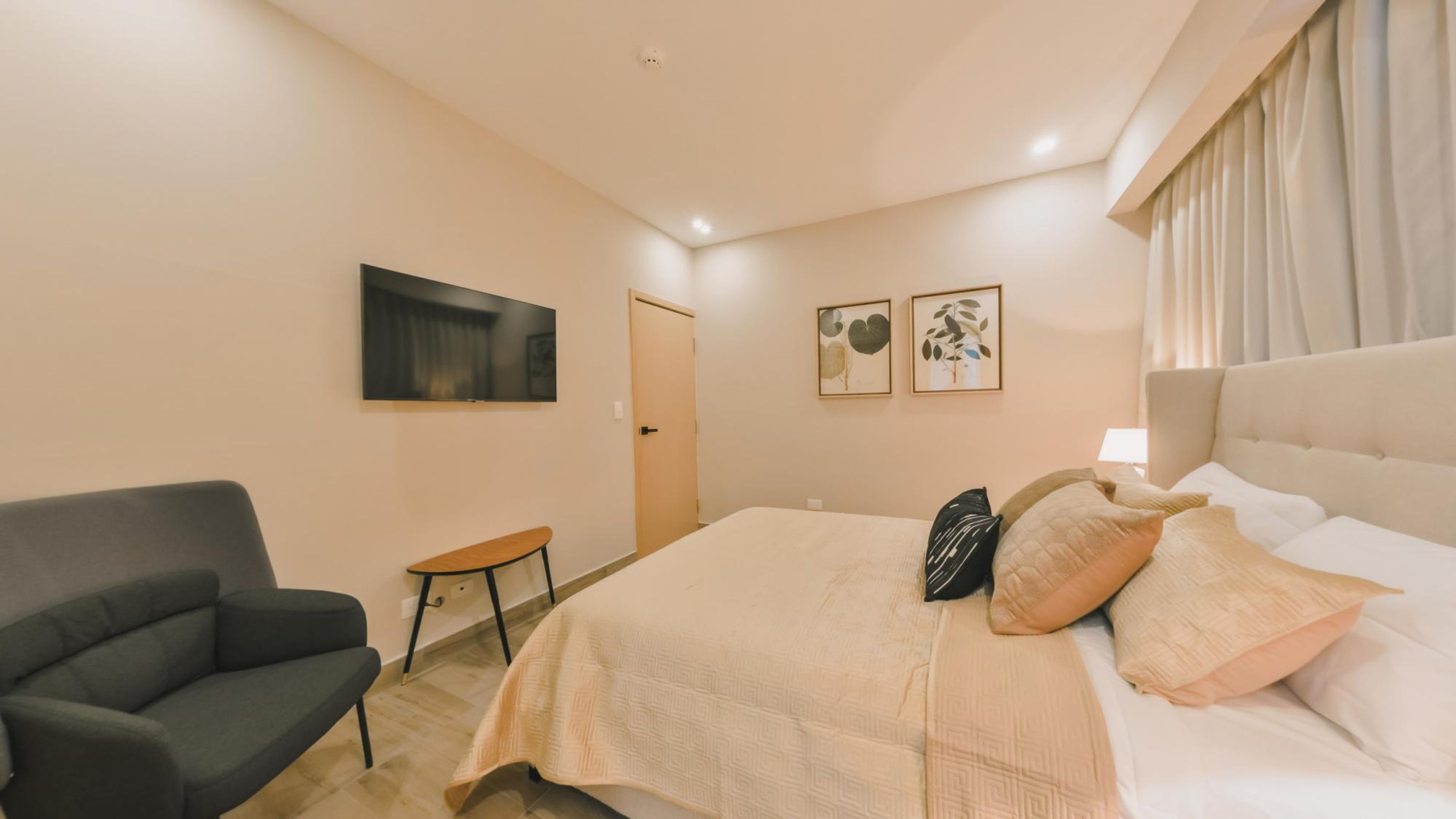 A hotel room with a bed, a chair, a small table, and two framed pictures on the wall.