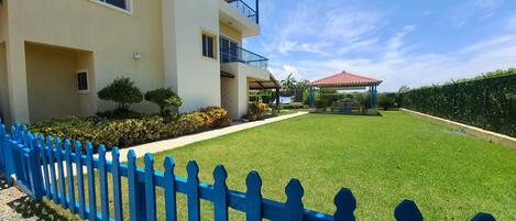 A two-story building with a blue picket fence, a well-maintained lawn, and a gazebo.
