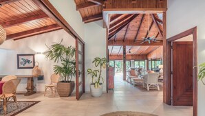 A spacious interior with high ceilings, wooden beams, and a mix of wicker furniture and potted plants. - 5BR 14 Guests Maid Included Casa de Campo (La Romana)