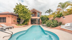 A swimming pool with lounge chairs, a two-story building, and tropical plants. - 5BR 14 Guests Maid Included Casa de Campo (La Romana)