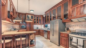 A kitchen with wooden cabinets, a stainless steel refrigerator, a gas stove, and a bar area with stools. - 5BR 14 Guests Maid Included Casa de Campo (La Romana)