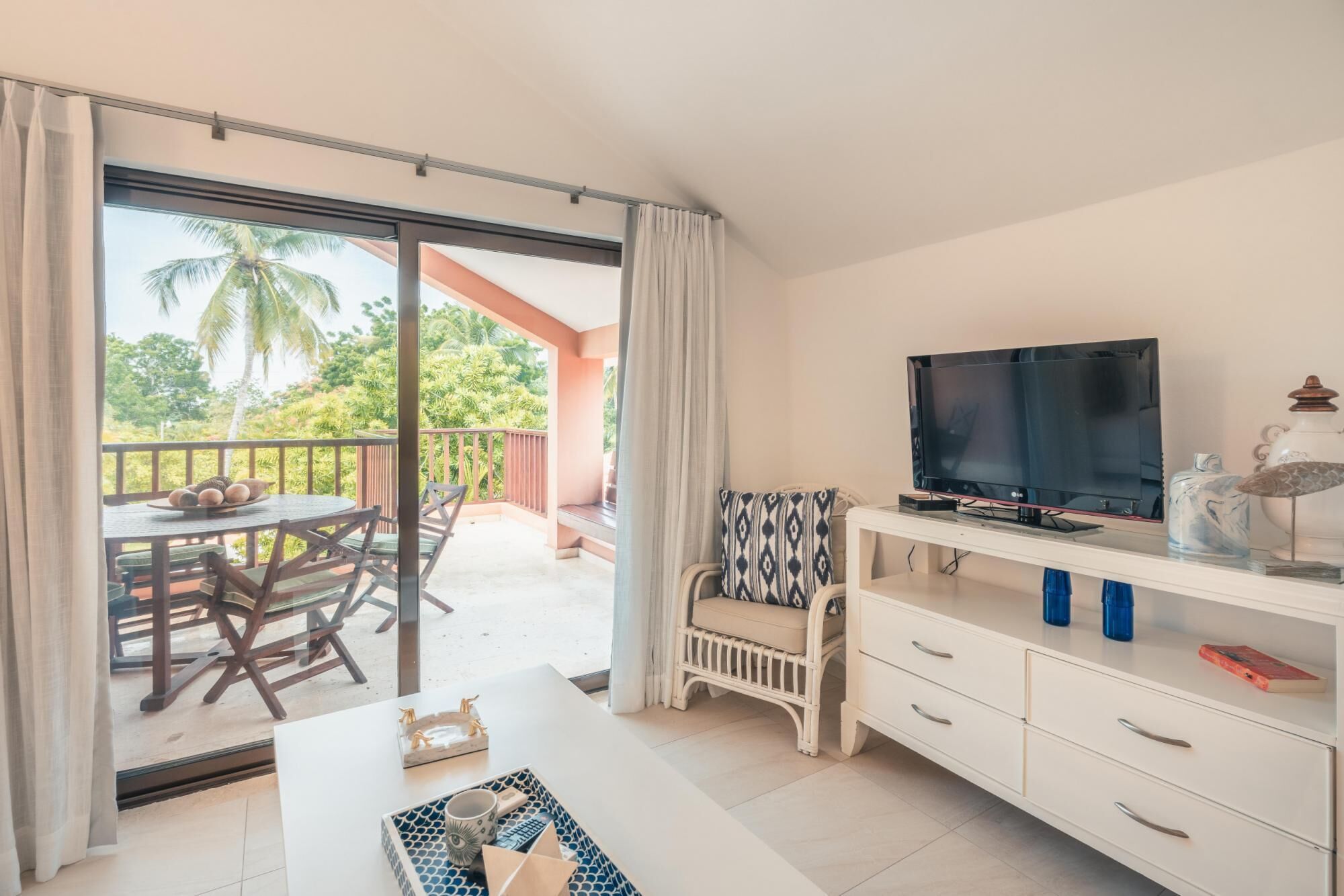 Une chambre avec un balcon, une télévision, une table à manger et un meuble blanc.