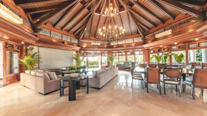 A spacious living area with a high ceiling, a chandelier, and a large TV. There are sofas, chairs, and a dining area with tables and chairs. - Luxurious Maison Larimar at Casa de Campo (La Romana)