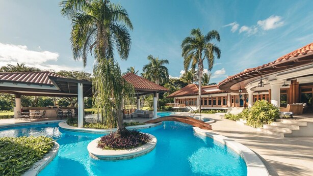 A resort pool area with palm trees, covered seating areas, and a clear blue pool. - Luxurious Maison Larimar at Casa de Campo (La Romana)