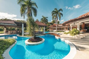 A resort pool area with palm trees, covered seating areas, and a clear blue pool. - Luxurious Maison Larimar at Casa de Campo (La Romana)