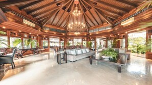 A spacious lobby with a high wooden ceiling, a central seating area with a sofa and chairs, and large windows allowing natural light. - Luxurious Maison Larimar at Casa de Campo (La Romana)
