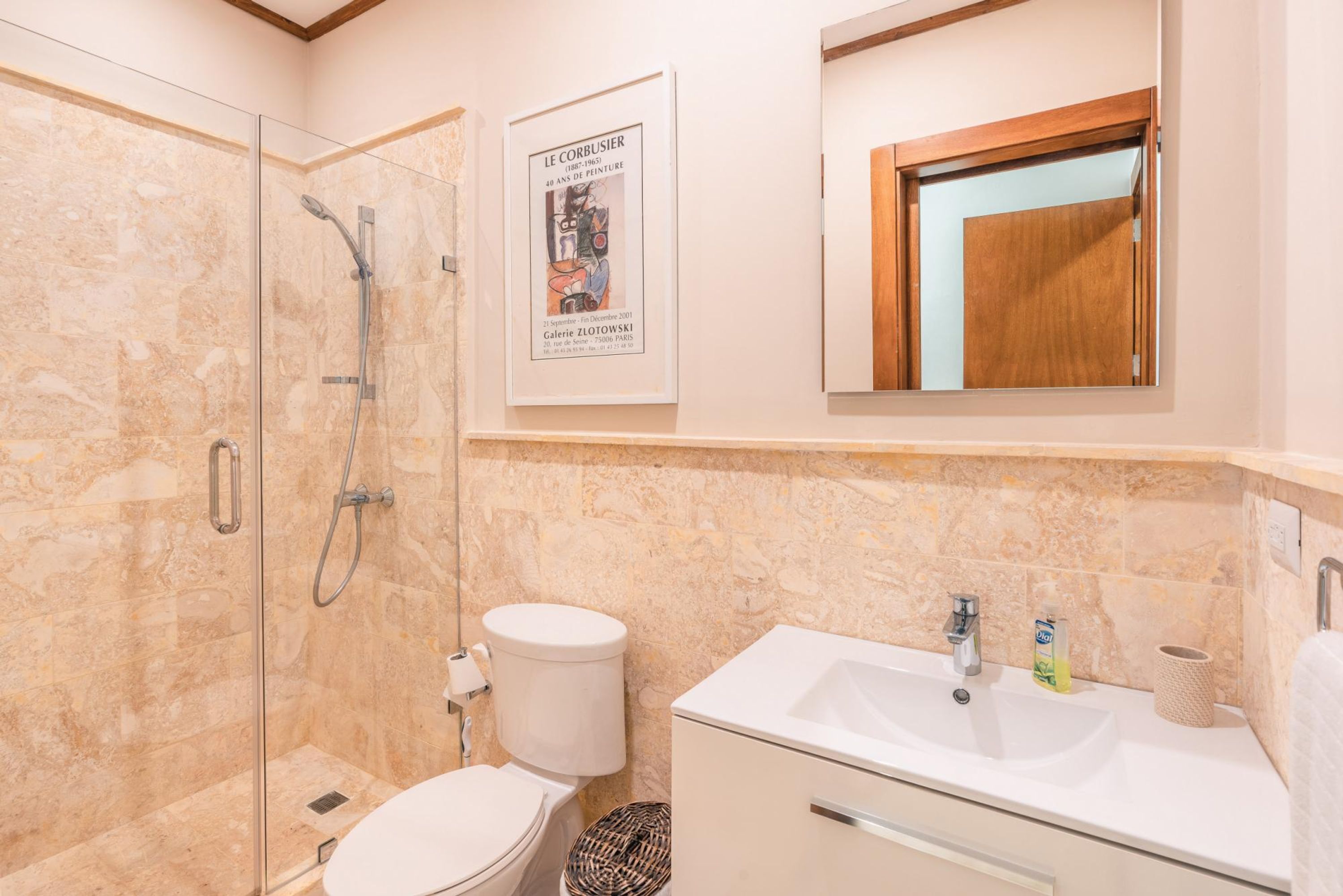 A bathroom with a glass-enclosed shower, a toilet, a sink, and a framed poster on the wall.