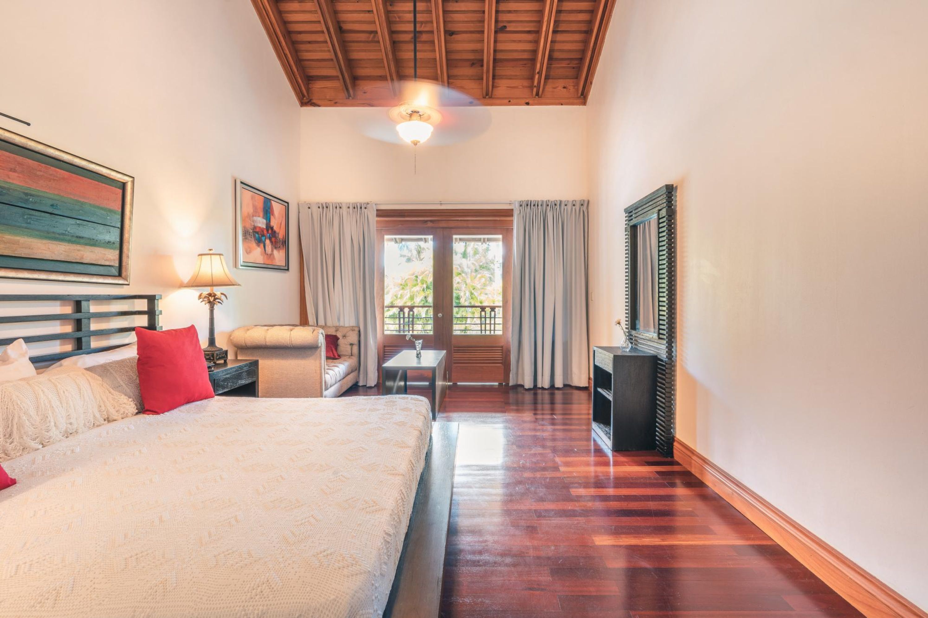 A hotel room with a large bed, a small table, a sofa, a ceiling fan, and a window with curtains.