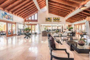 Eine geräumige Lobby mit hohen Decken, Holzbalken und großen Fenstern. Es gibt mehrere Sitzbereiche mit Sofas und Tischen.
